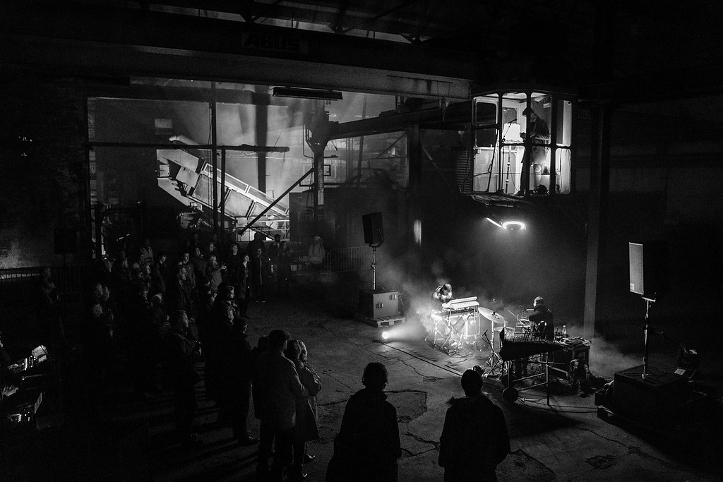 Konsert i et mørkt industrilokale. Foto.