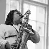 Nærbilde av musiker Lady Albatross som spiller saksofon med stor innlevelse. Bak henne er store vinduer med mange sprosser. Froskeperspektiv. Foto.