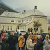 En folkemengde har samlet seg på Lindeplassen i Odda. Et lysegrønt hus og høstfargede fjellsider utgjør bakgrunnen av bildet. Foto.